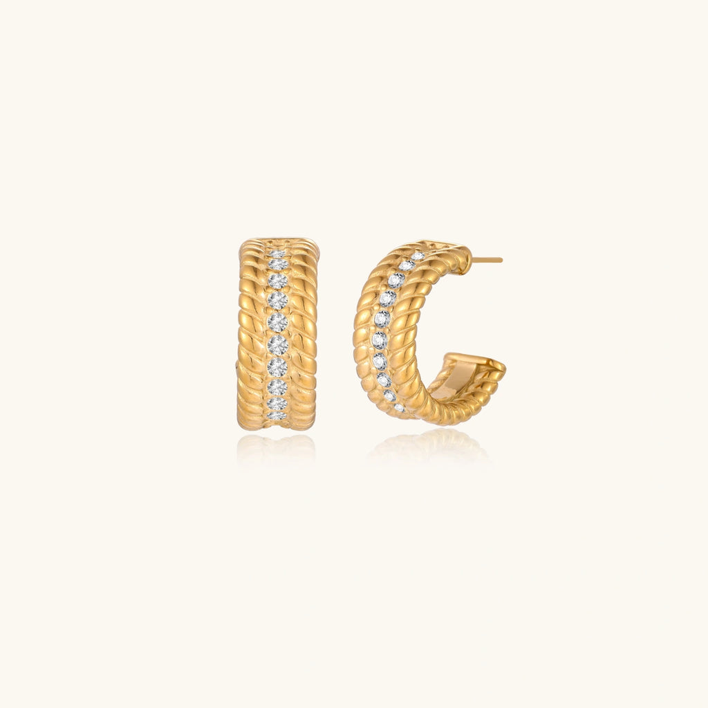 Textured gold huggie hoop earrings with raised ribbed rows creating dimensional sculptural design on cream background